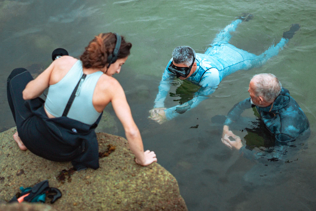 Femme avec casque et micro sur un rocher face à une femme et un homme dans l'eau