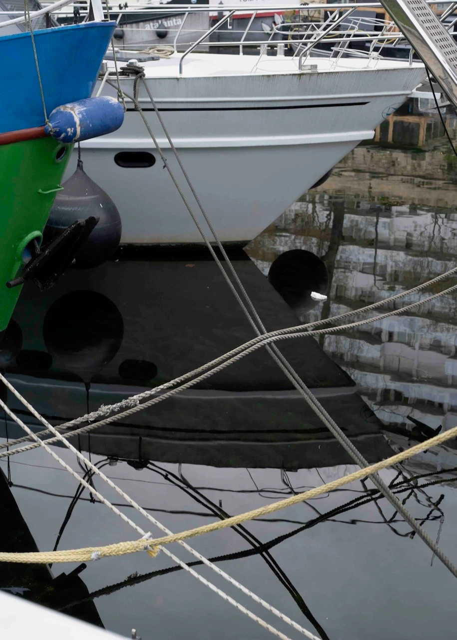 Proues de plusieurs bateaux amarrés côte à côte dans un port, avec leurs reflets dans l'eau calme