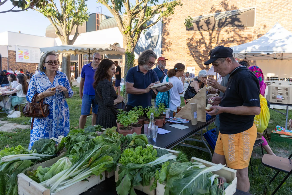 Des visiteurs découvrent un stand de légumes frais installé sur la pelouse de La Garance. Des cagettes remplies de salades, blettes, poireaux et autres légumes sont disposées au premier plan.