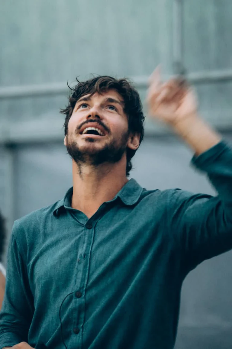 Portrait de Gael Faure, chemise verte, souriant et regardant vers le ciel, un bras levé