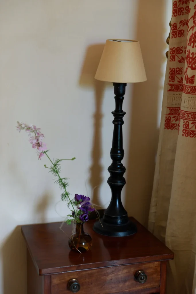 Table de chevet en bois foncé avec, posés dessus, une lampe sur pied et un soliflore.