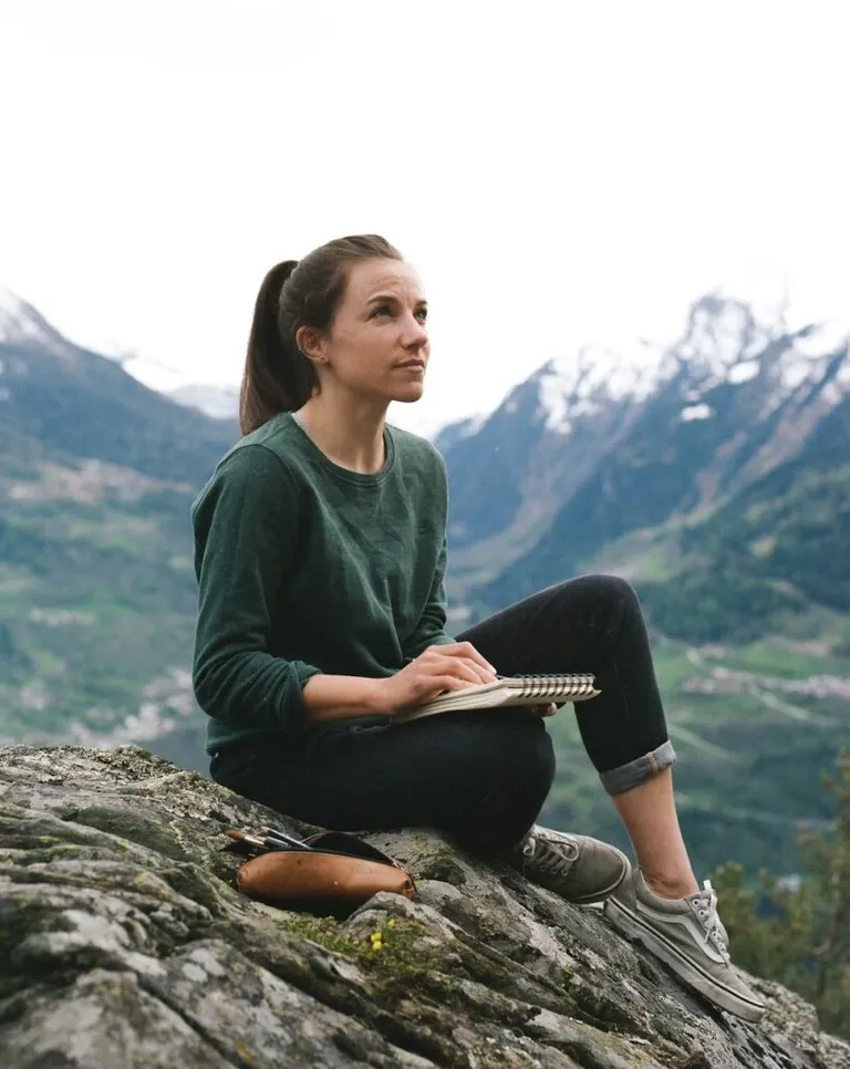 Lauriane Miara assise sur un rocher avec son carnet à dessin avec la montagne en fond
