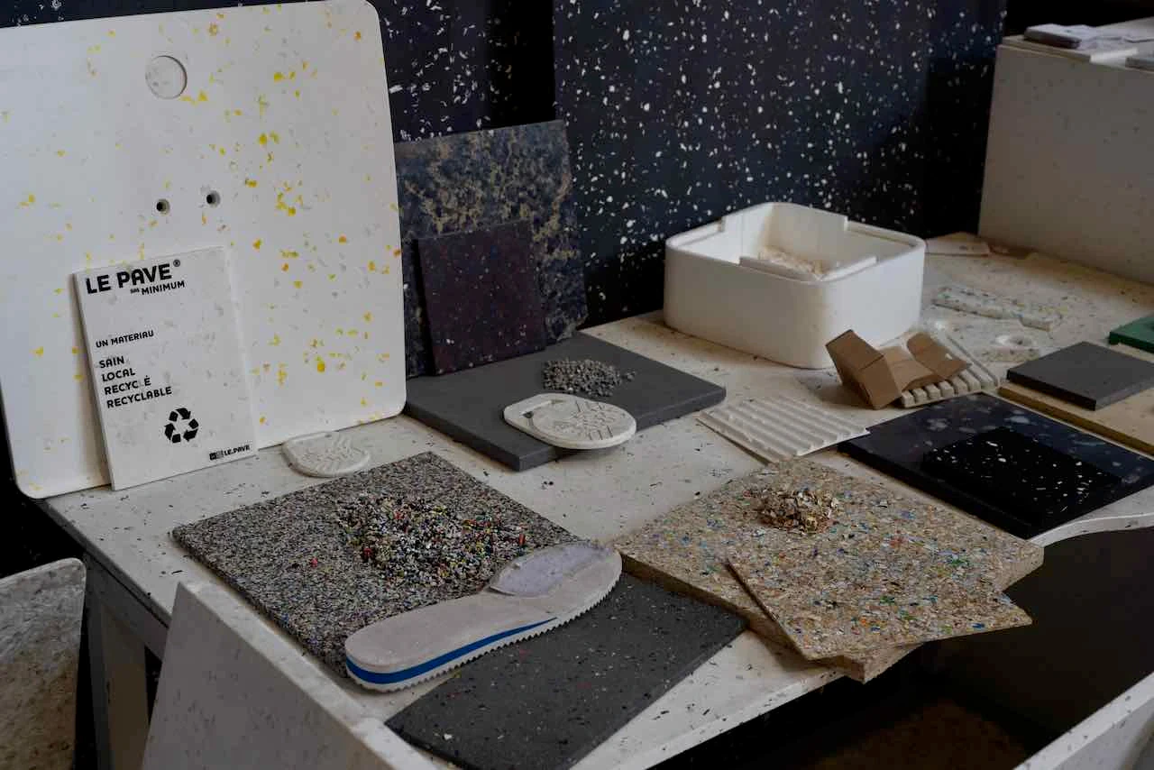 Table couverte d'échantillons de panneaux en plastique recyclé de différentes couleurs et textures, avec le logo Le Pavé.
