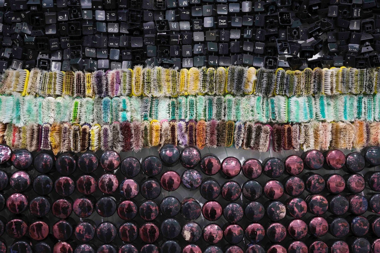 Assemblage de touches de clavier noires, de brosses à dents multicolores et de capsules métalliques roses formant une composition en bandes horizontales
