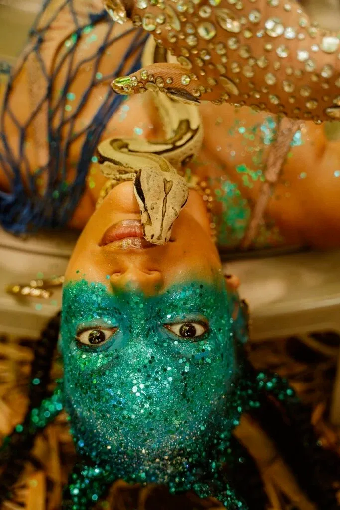 Visage d'une femme maquillée avec des paillettes vertes et un serpent posée sur elle