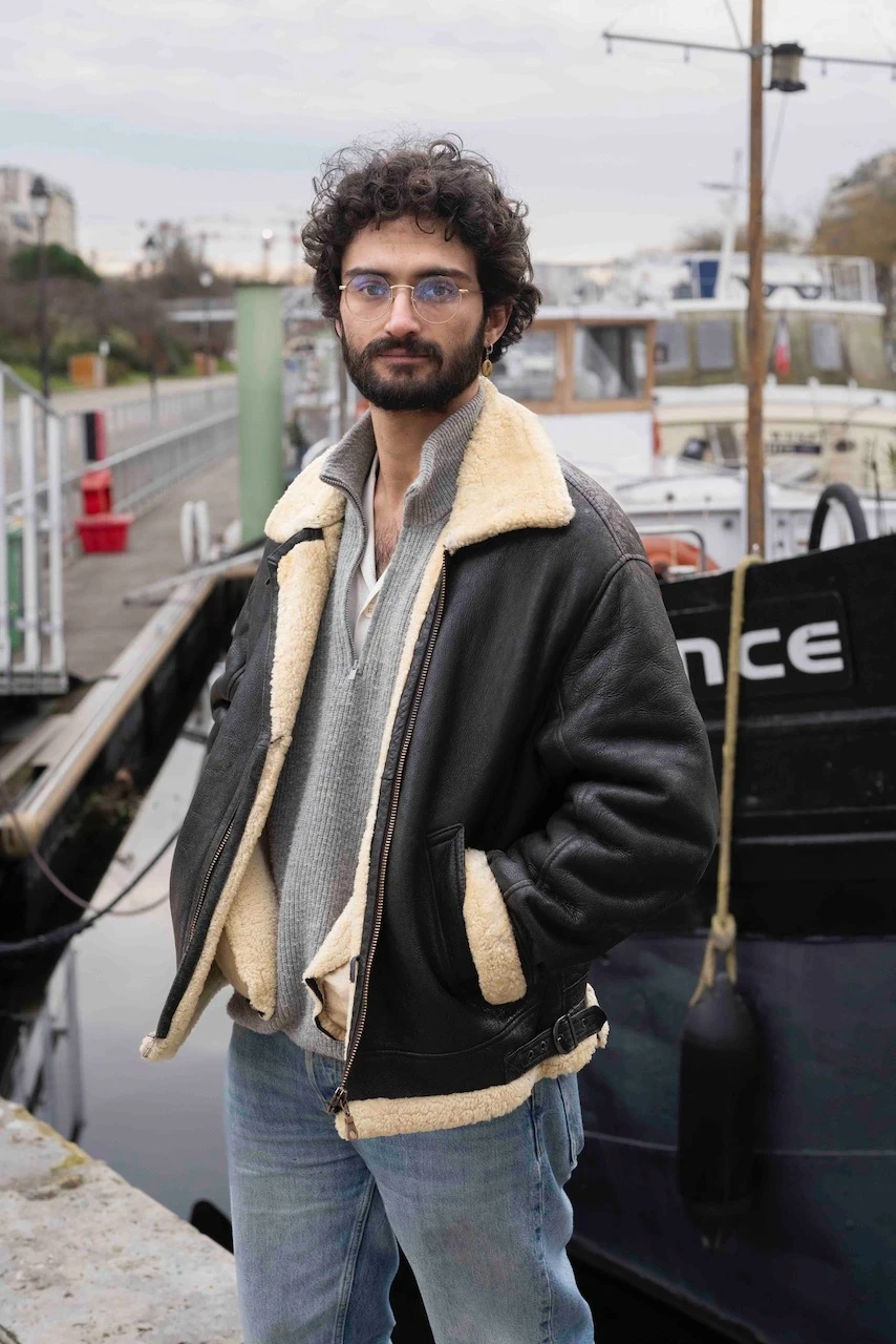 Portrait de Pedro de la Patellière, biologiste marin aux cheveux bouclés et lunettes rondes, posant sur un quai devant des péniches.