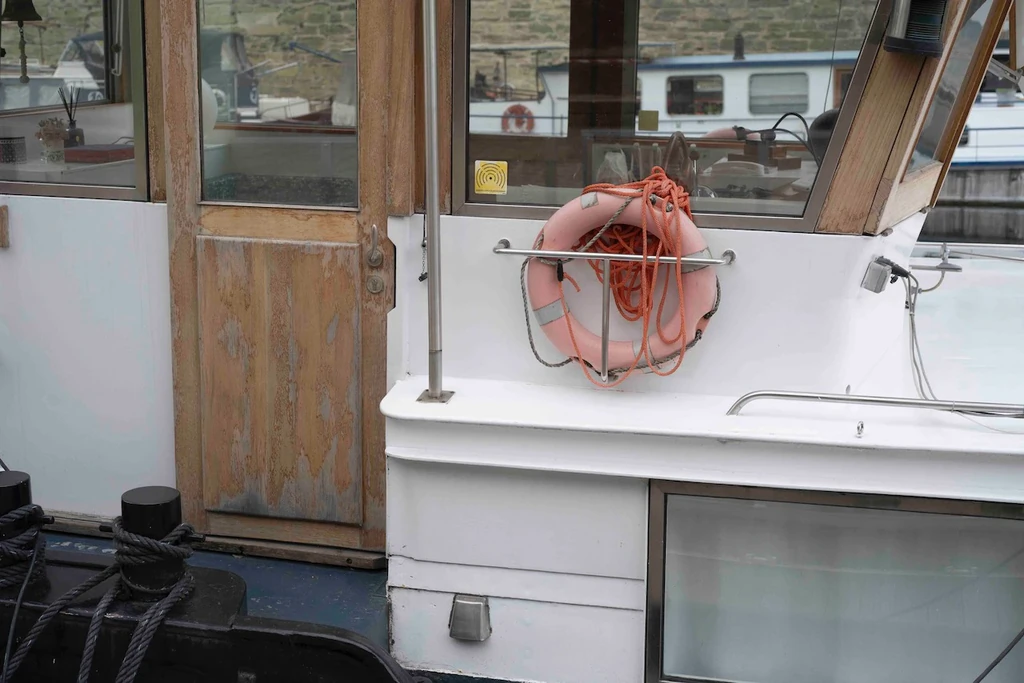 Bouée de sauvetage orange accrochée à la cabine blanche d'une péniche, à quai