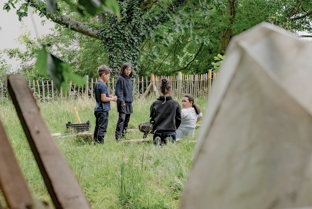 Au second plan, cinq enfant assis en cercle discutent assis dans l'herbe