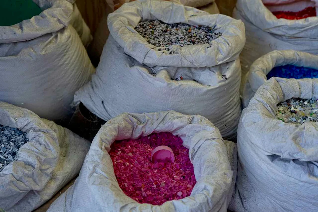 Sacs de plastique broyé aux couleurs vives — rose, bleu, gris — prêts à être transformés en panneaux.