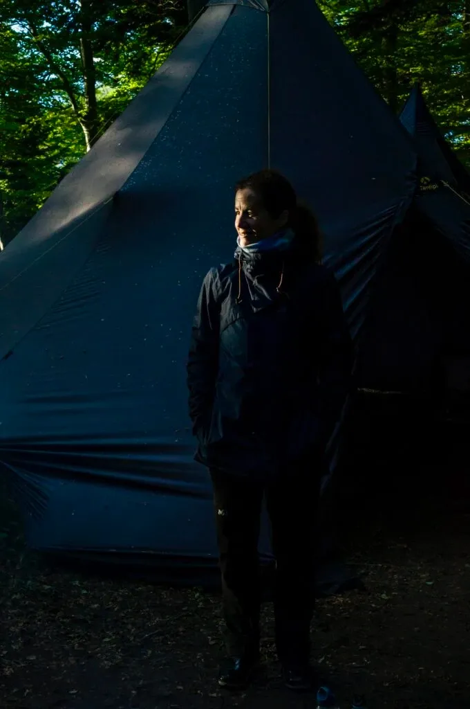 Randonneuse debout devant une tente de bivouac dans une forêt